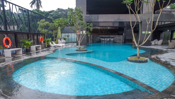 A swimming pool with a waterfall feature, surrounded by lounge chairs and potted plants. - Comfort Stay 2Br At L'Avenue Pancoran Apartment (Jakarta)