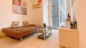 A modern living room with a sofa, a glass coffee table, and a white cabinet with a plant. - Comfort Stay 2Br At L'Avenue Pancoran Apartment (Jakarta)