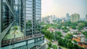 A high-rise building with a glass facade, a rooftop garden, and a view of a cityscape with residential areas and greenery. - Comfort Stay 2Br At L'Avenue Pancoran Apartment (Jakarta)