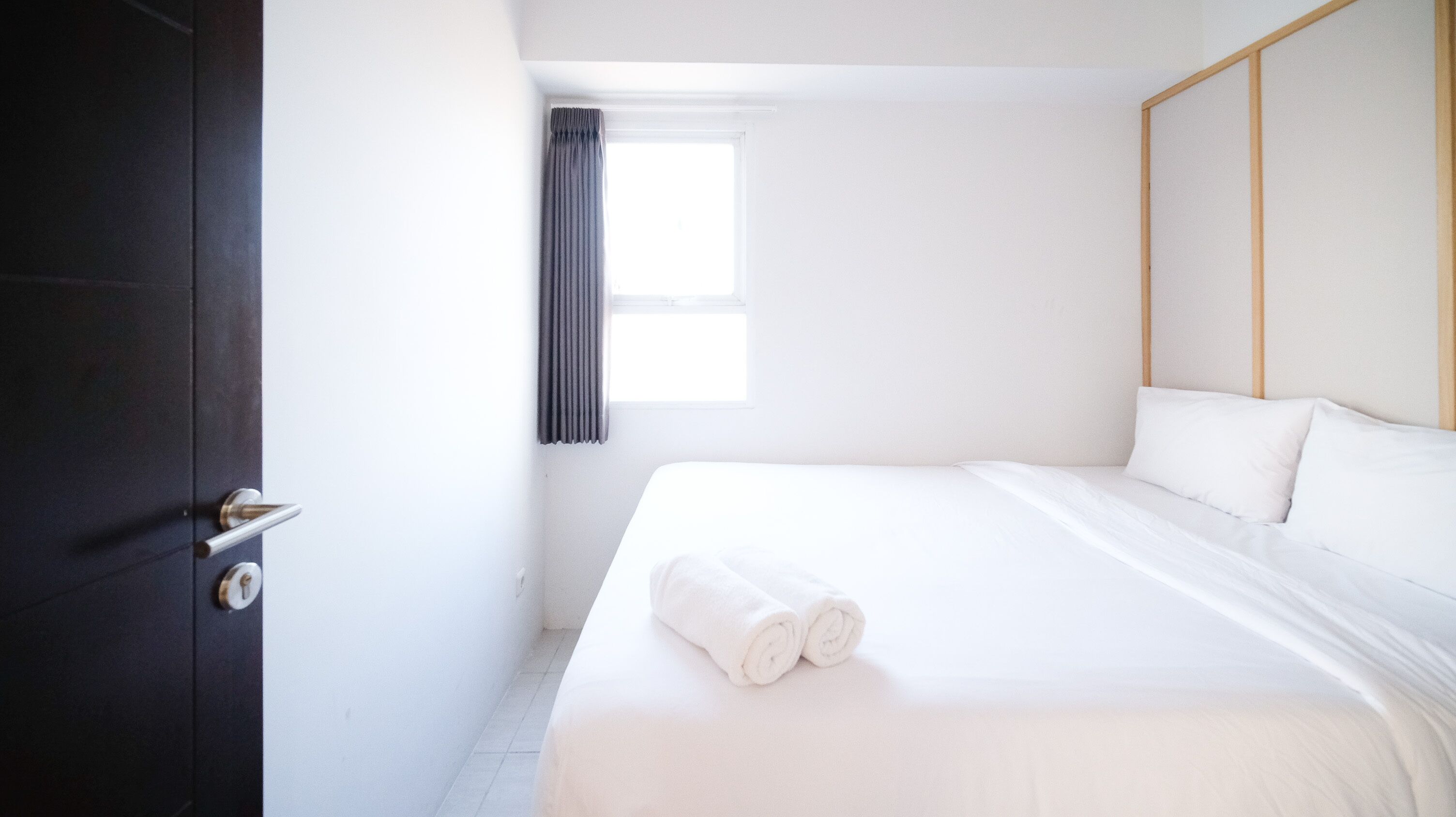 Habitación de hotel con cama, ventana con cortinas, puerta y cabecero de madera.
