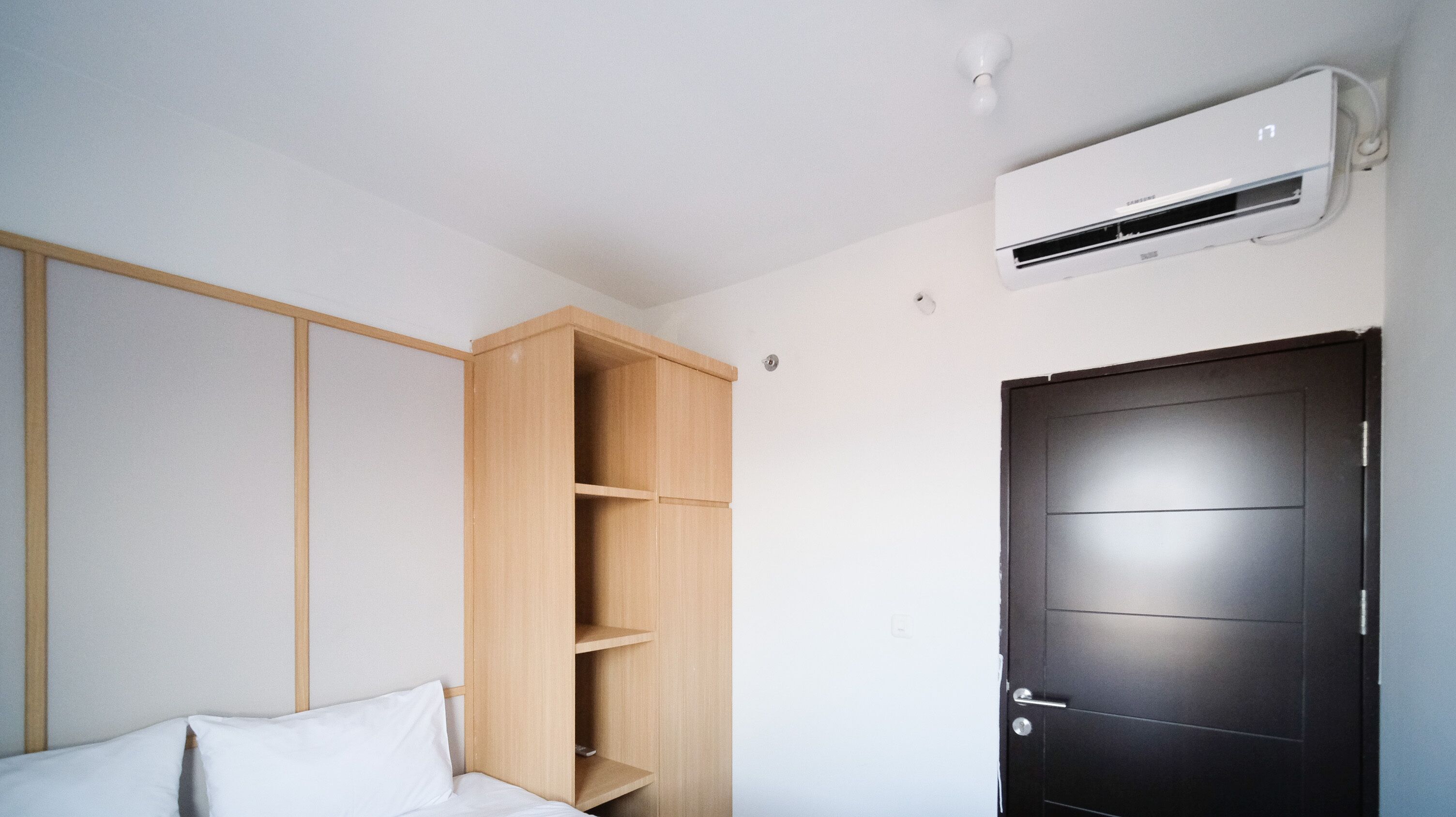 A bedroom with a bed, a wooden wardrobe, a black door, and a wall-mounted air conditioner.