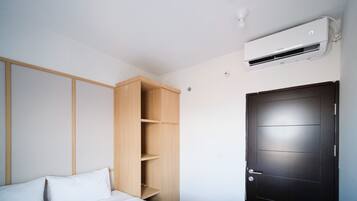 A bedroom with a bed, a wooden wardrobe, a black door, and a wall-mounted air conditioner.