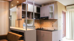 Una cocina compacta con electrodomésticos modernos, horno integrado y lavamanos. Hay una zona de comedor con un sofá marrón y una mesa.