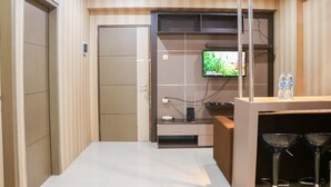 Una habitación de hotel moderna con una televisión de pantalla plana montada en la pared, un escritorio pequeño con una silla, y una zona de bar con taburetes.