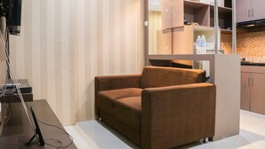 Una sala de estar moderna con un sofá marrón, televisión y una cocina con armarios y encimera.