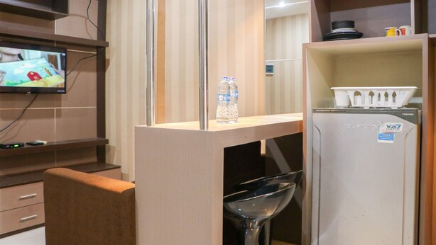 Habitación de hotel compacta con kitchenette, televisor montado en la pared, un refrigerador pequeño y una zona de comedor con una silla y una mesa.