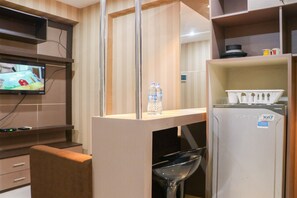 Habitación de hotel compacta con kitchenette, televisor montado en la pared, un refrigerador pequeño y una zona de comedor con una silla y una mesa.