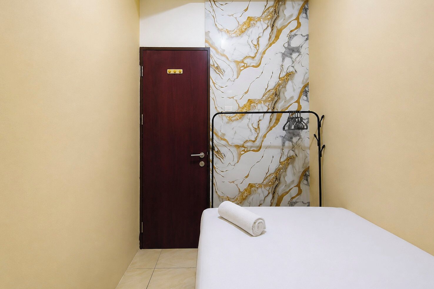 A small hotel room with a single bed, a wooden door, and a marble-patterned wall.