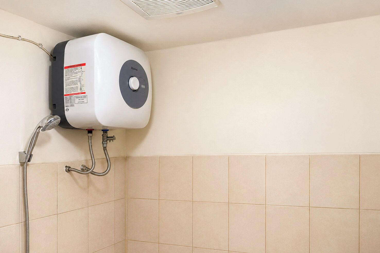 A bathroom with a wall-mounted water heater, a showerhead, and beige tiles.
