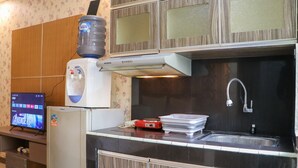 A compact kitchen with a water dispenser, a microwave, a refrigerator, a sink, and a television displaying 'Avengers'. - Spacious Studio At Gateway Ahmad Yani Cicadas Apartment (Bandung)