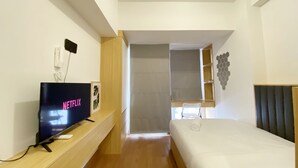Et moderne hotelværelse med et fladskærms-tv, der viser 'NETFLIX', et trænatbord, en seng med sengegavl og en gang, der fører til et badeværelse.