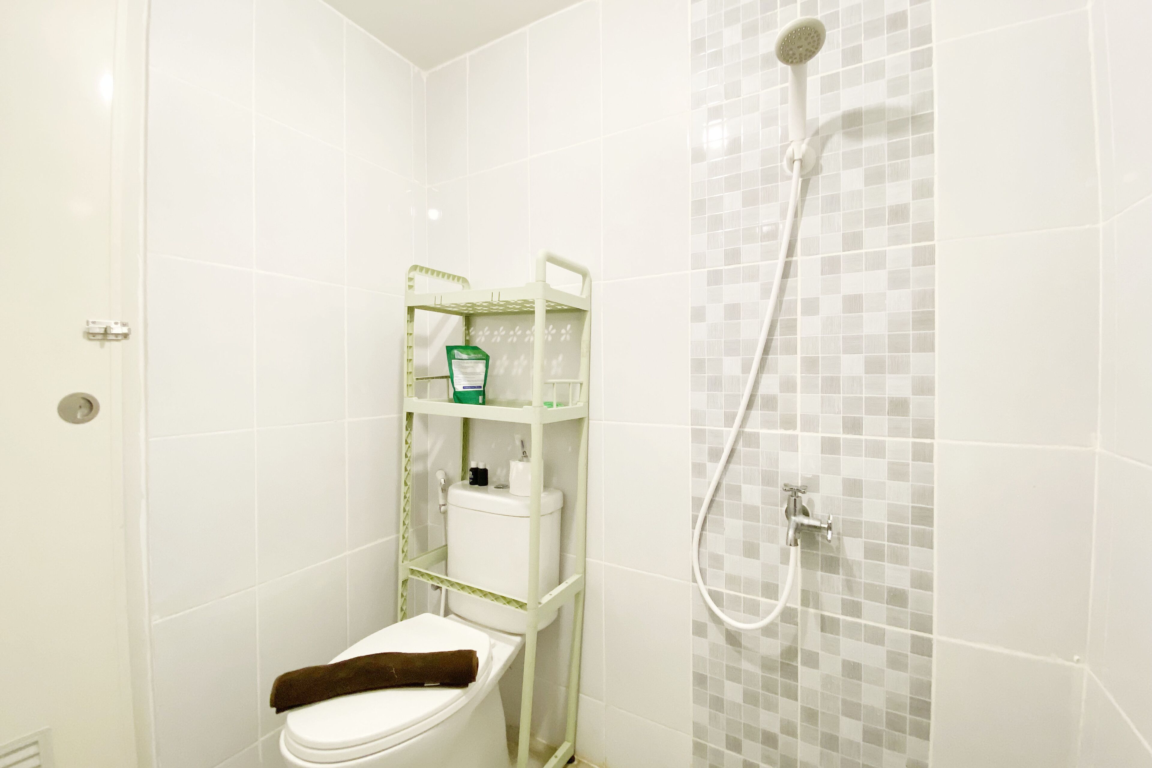 A bathroom with a toilet, a shower, and a shelf with toiletries.