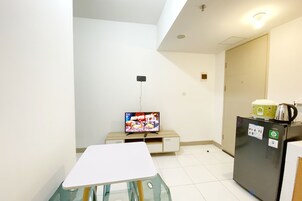 Una kitchenette pequeña equipada con un refrigerador, microondas y cafetera. En primer plano, una mesita y una silla.