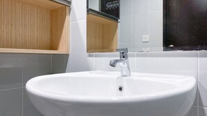 A white bathroom sink with a chrome faucet, tiled walls, and a wooden vanity cabinet. - Comfort And Enjoy Living Studio Casa De Parco Apartment (Pagedangan)