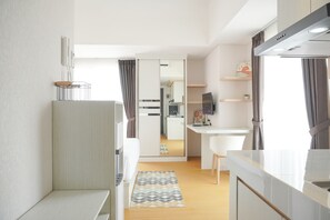 A modern kitchen with a white countertop, a built-in stove, and a dining area with a white chair and table. - Comfort And Enjoy Living Studio Casa De Parco Apartment (Pagedangan)