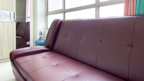 A brown leather sofa in a room with a large window, a blue water bottle, and a wooden wardrobe.
