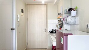 A compact kitchen with a refrigerator, a sink, and a countertop. There is a door with a phone on the wall and a red bucket near the sink.