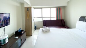 A hotel room with a bed, a TV, a desk, a wardrobe, and a window with curtains.