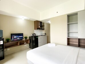 Ein modernes Hotelzimmer mit Bett, Fernseher, einer Küchenzeile und einem Kleiderschrank.