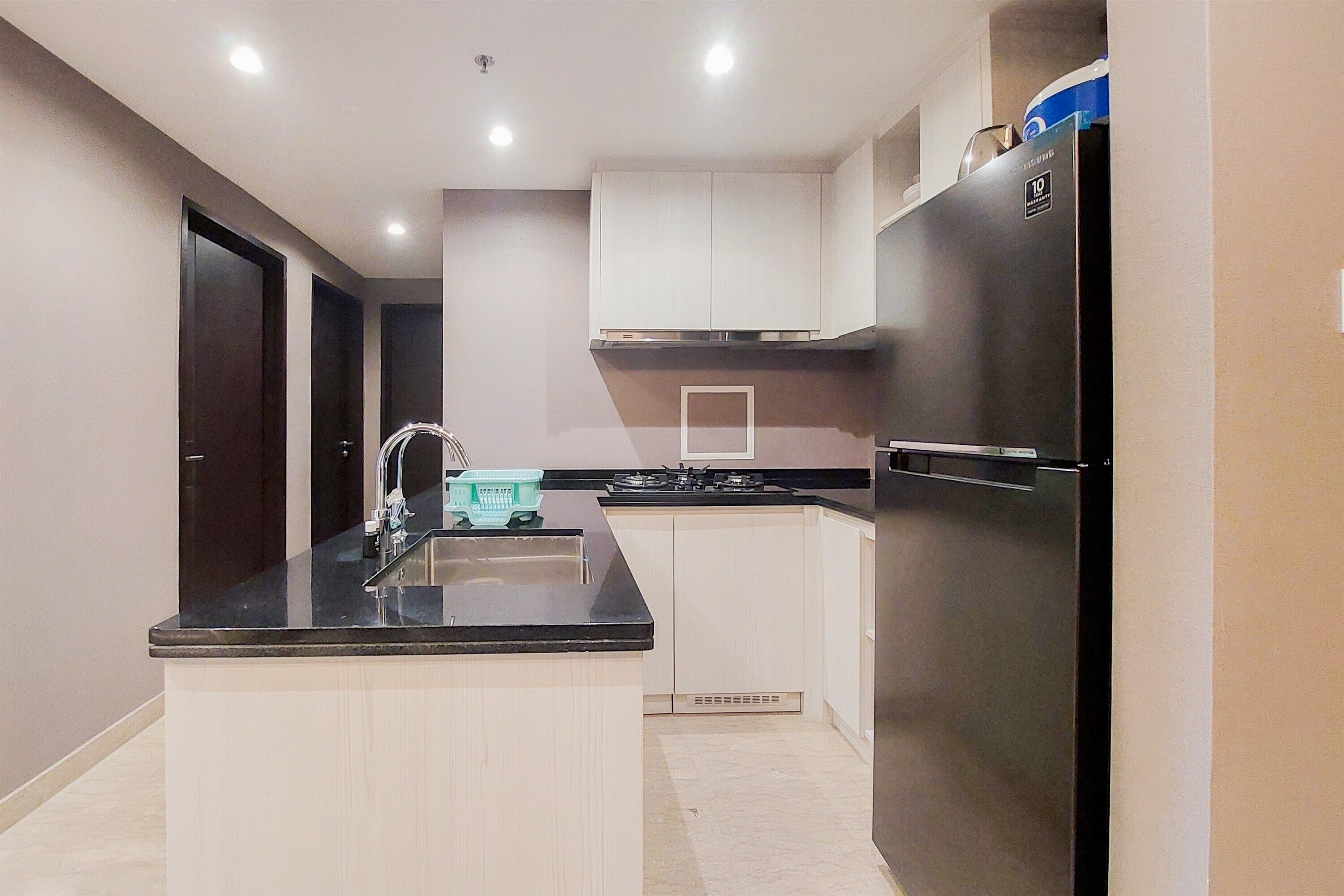 Una cocina moderna con un refrigerador negro, gabinetes blancos y una encimera negra.