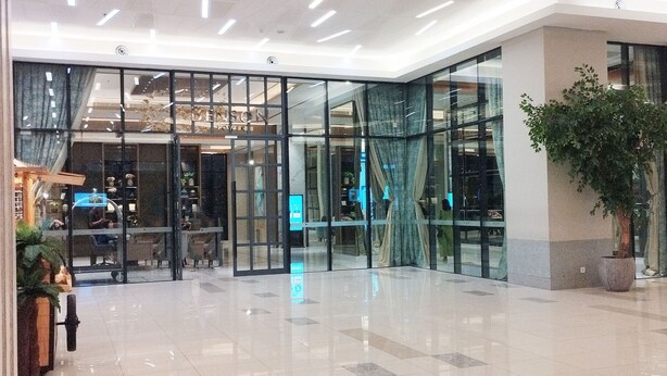 A modern hotel lobby with glass doors, a reception desk, and a large potted plant. - Modern And Cozy Studio At Benson Supermall Mansion Apartment (Surabaya)
