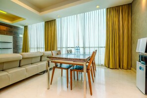 A modern living room with a glass-top dining table, beige sofa, and a TV on a stand.