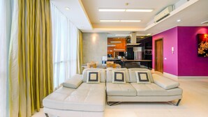 A modern living room with a sectional sofa, a dining area, and a kitchen in the background. - Homey Penthouse 3Br With Extra Room Kemang Village Apartment (Jakarta)
