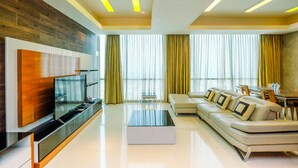 A modern living room with a flat-screen TV, a sofa, a coffee table, and a dining area with a table and chairs. - Homey Penthouse 3Br With Extra Room Kemang Village Apartment (Jakarta)