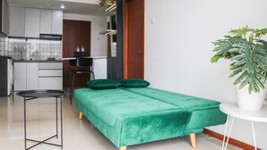 A compact room with a green bed, a small table, a potted plant, and a kitchenette in the background. - Spacious 3Br With Good View At Gateway Pasteur Apartment (Cimahi)