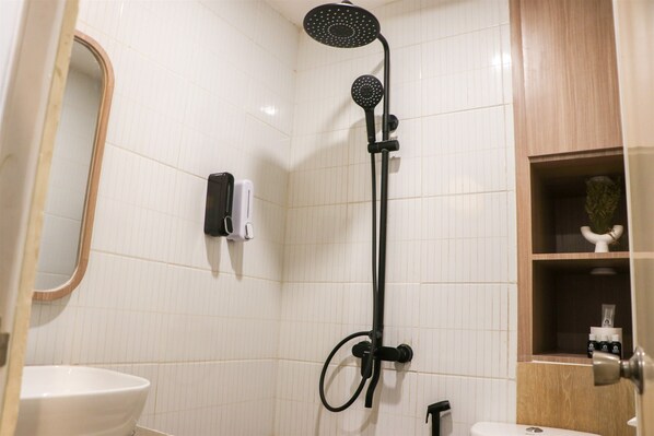Un baño con un lavamanos blanco, un espejo, una ducha con manguera negra y un inodoro.