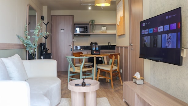 A compact living space with a sofa, a coffee table, a TV, a microwave, and a small dining area. - Brand New 2Br At Tamansari Panoramic Apartment (Bandung)