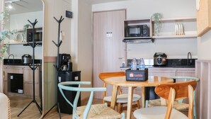 A compact kitchen with a microwave, coffee maker, and a small refrigerator. There is a dining table with chairs and a mirror reflecting the kitchen. - Brand New 2Br At Tamansari Panoramic Apartment (Bandung)
