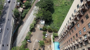 An aerial view of a multi-story building with a swimming pool, parking area, and a railway track running parallel to the street. - Brand New 2Br At Tamansari Panoramic Apartment (Bandung)