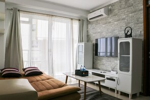 A modern living room with a sofa, a flat-screen TV, a white cabinet, and an air conditioning unit on the wall. - Minimalist And Cozy 2Br At Gateway Pasteur Apartment (Cimahi)