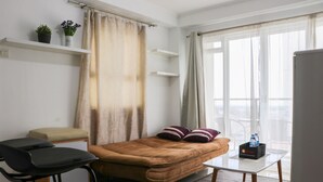 Un dormitorio con cama, escritorio, silla, un pequeño sofá y balcón con vistas.