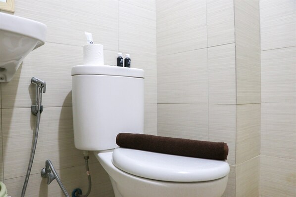 A white toilet with a brown towel on the seat, a white sink, and a shower head.