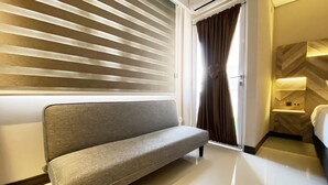Een moderne hotelkamer met een bank, een bed, een kaptafel met spiegel en een raam met zonwering.