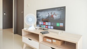 Ein modernes Wohnzimmer mit Flachbildfernseher, einem weißen Ventilator und einer Holzunterhaltungseinheit.