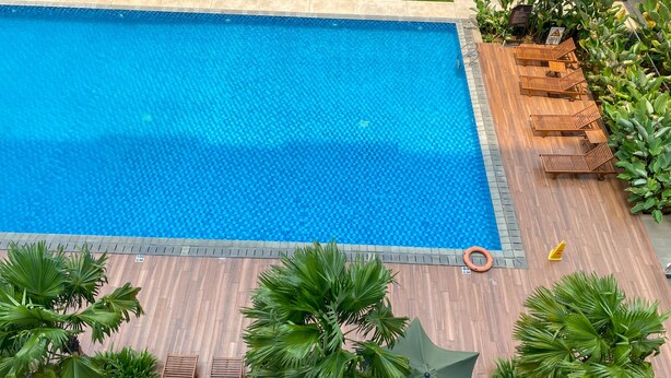 Ein rechteckiger Swimmingpool mit Fliesenrand, umgeben von einer Holzterrasse und üppigem Grün.