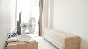 Ein Zimmer mit Schreibtisch, Computer, Ventilator und einer Couch.