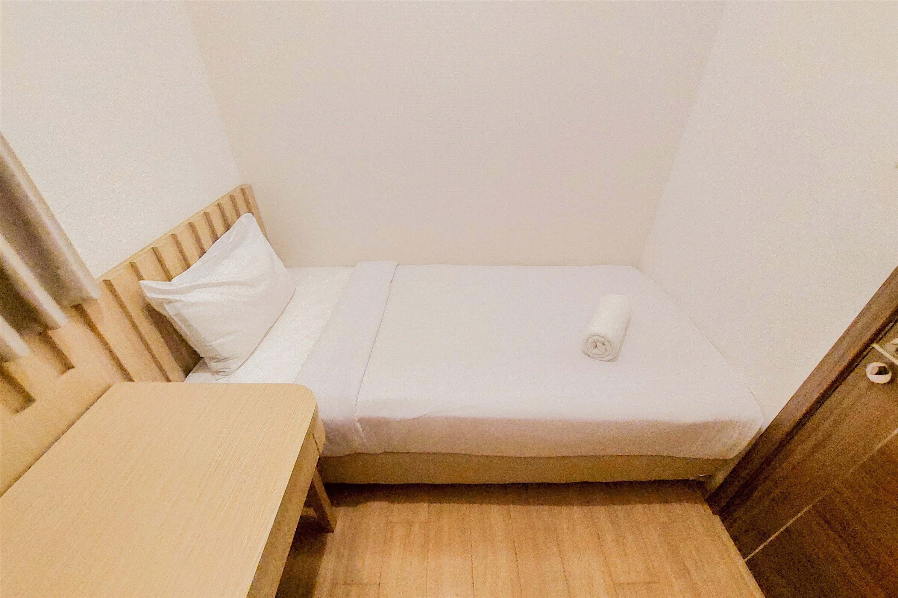 Ein kleines Zimmer mit einem Einzelbett, einem Holzkopfstück, einem Holztisch und einem weißen Lattenrost.