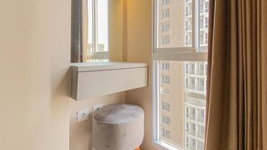 Ein kleines, modernes Badezimmer mit einem weißen Waschtisch, einem runden Hocker und einem Fenster mit Blick auf hohe Gebäude.