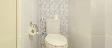 Un baño pequeño y blanco con inodoro, dispensador de papel higiénico y cabezal de ducha.