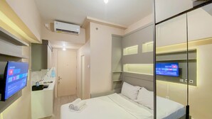 Ein modernes Hotelzimmer mit Bett, einem an der Wand befestigten Fernseher, einem kleinen Schreibtisch mit Spüle und einer Klimaanlage.