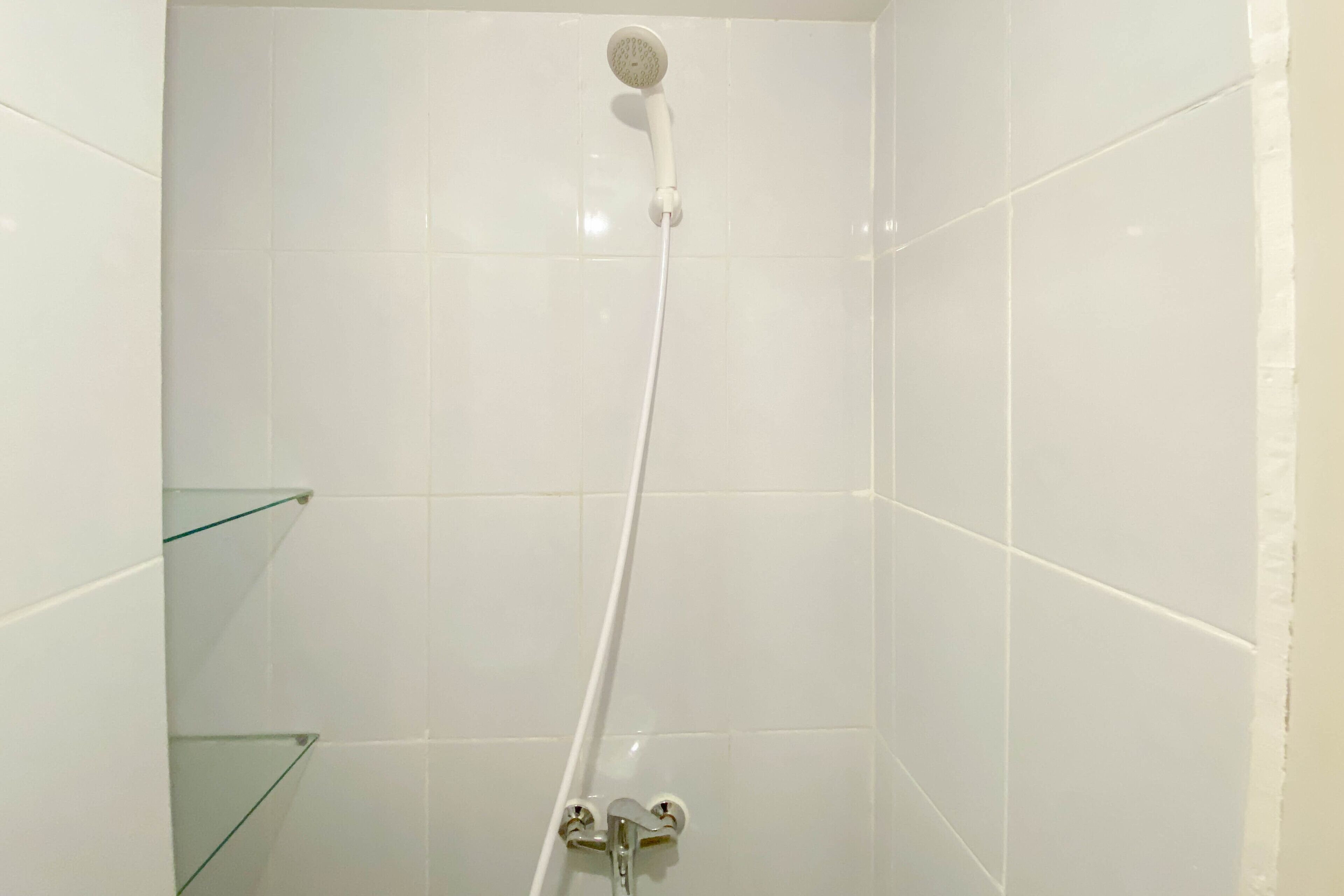 A shower with a handheld showerhead and a wall-mounted faucet.