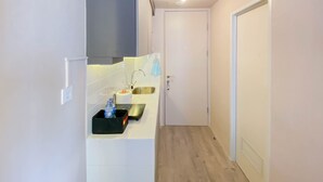 Ein schmales Entree mit einer Küchenzeile links, ausgestattet mit einem Spülbecken, einer Arbeitsplatte und einem blauen Handtuch. Eine weiße Tür ist rechts sichtbar.