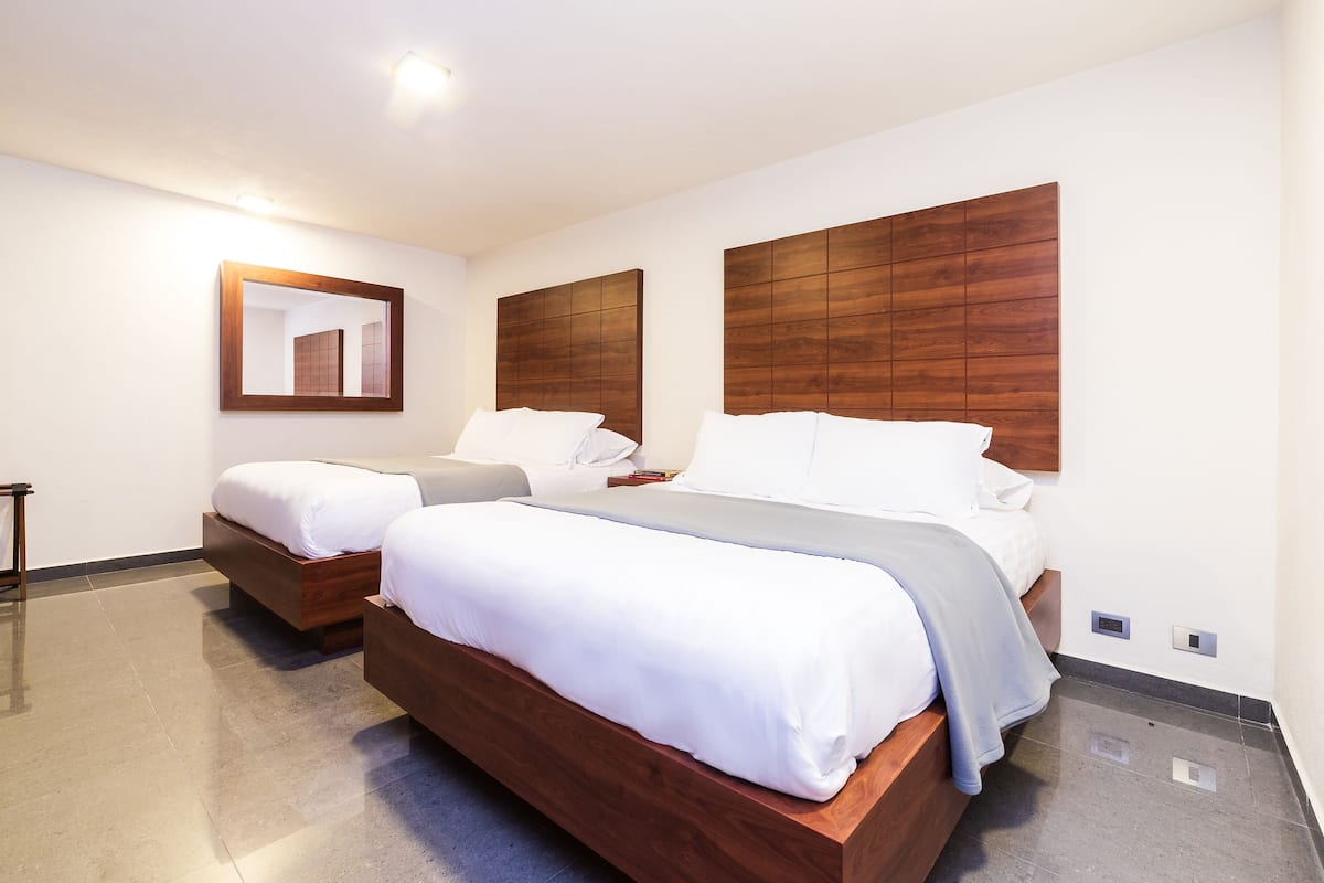 A hotel room with two wooden beds, a large mirror, and a modern design.