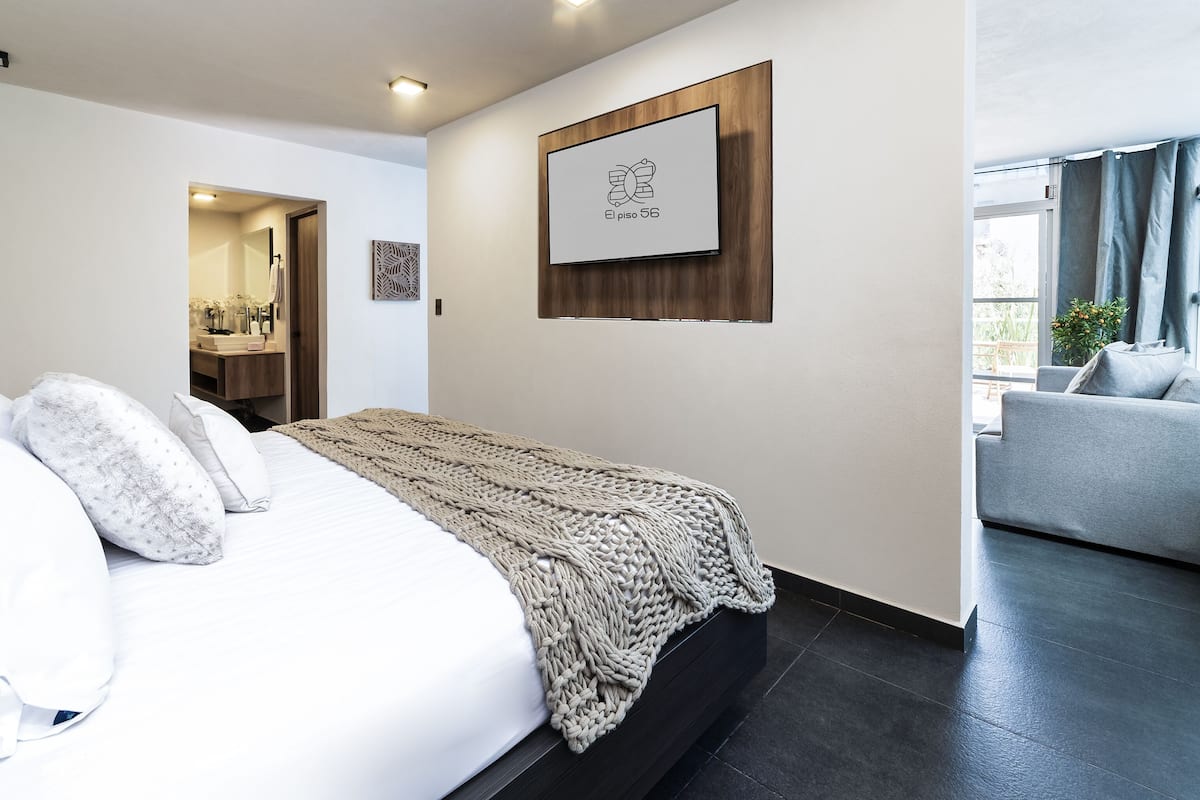 A modern bedroom with a bed, a bedside table, a wall-mounted TV, and a view of the outside.