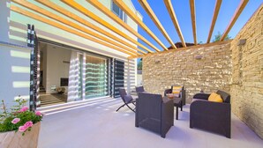 An outdoor patio with wicker furniture, a stone wall, and a view of the interior through a glass door. - Villa Amarie (Kvarner - Risika) (Risika)