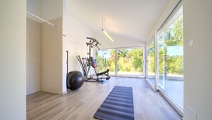 A spacious room with a large sliding glass door leading to a balcony, a wooden floor, a black exercise mat, and fitness equipment including a stationary bike and a rowing machine. - Villa Amarie (Kvarner - Risika) (Risika)